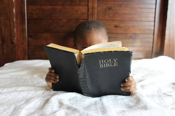 "Boy reading Bible while laying on bed" Photo by Samantha Sophia on Unsplash